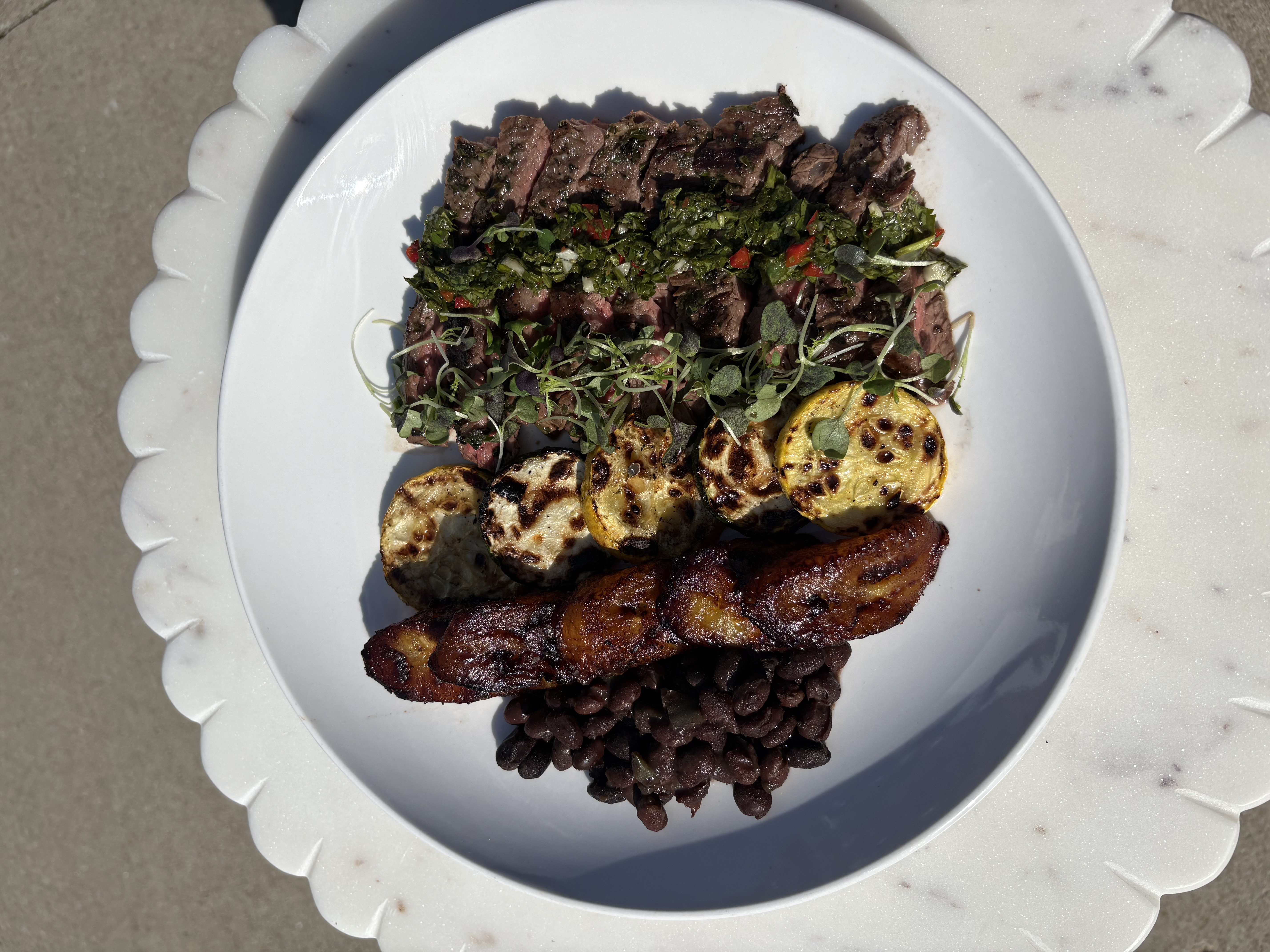 Chimichurri grass-fed skirt steak on white plate with black beans, sweet plantains and garlic zucchini